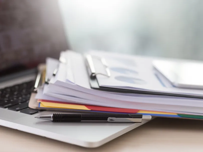 Laptop with a stack of documents and folders on a desk