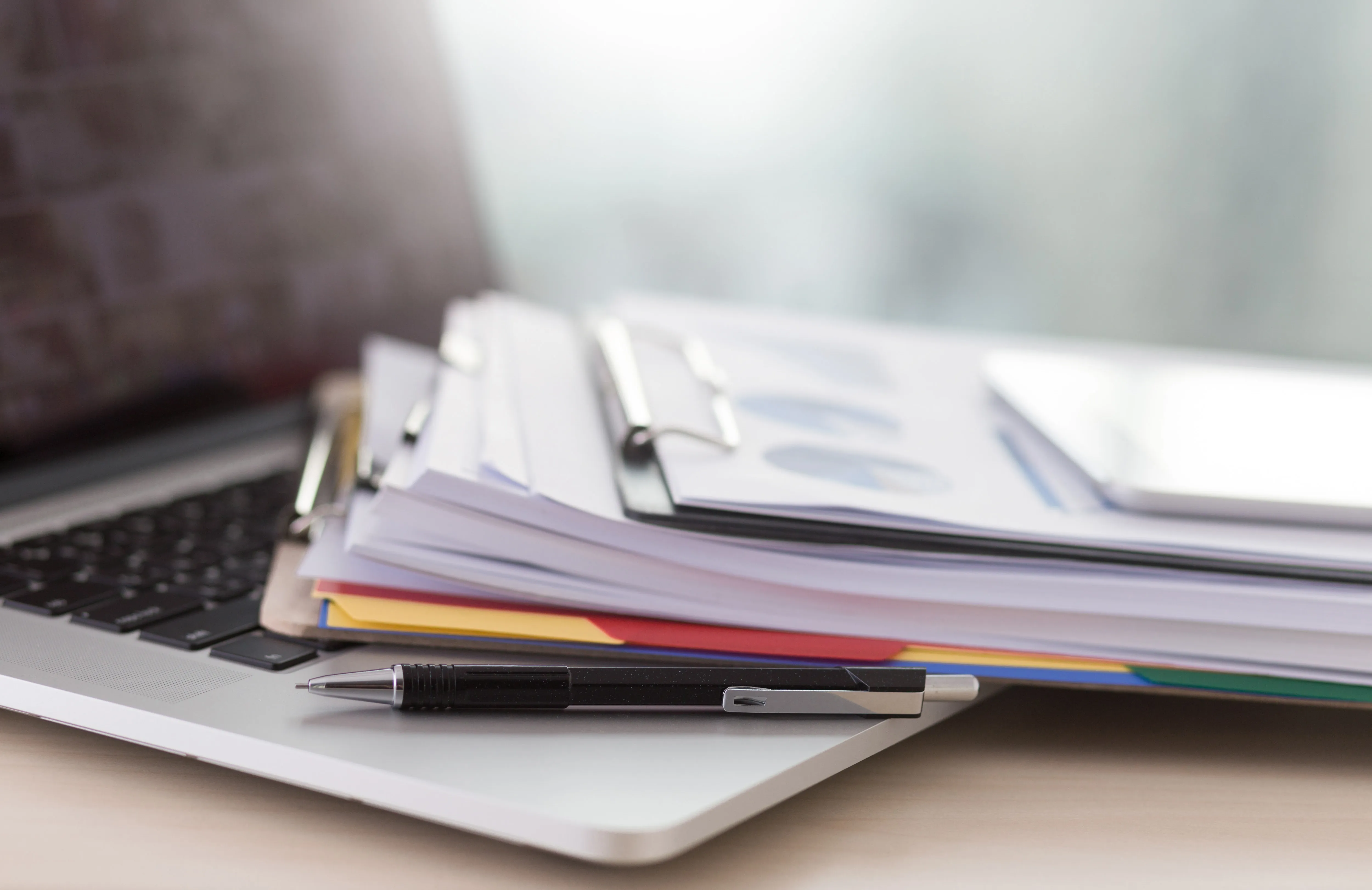 Laptop with a stack of documents and reports on a desk