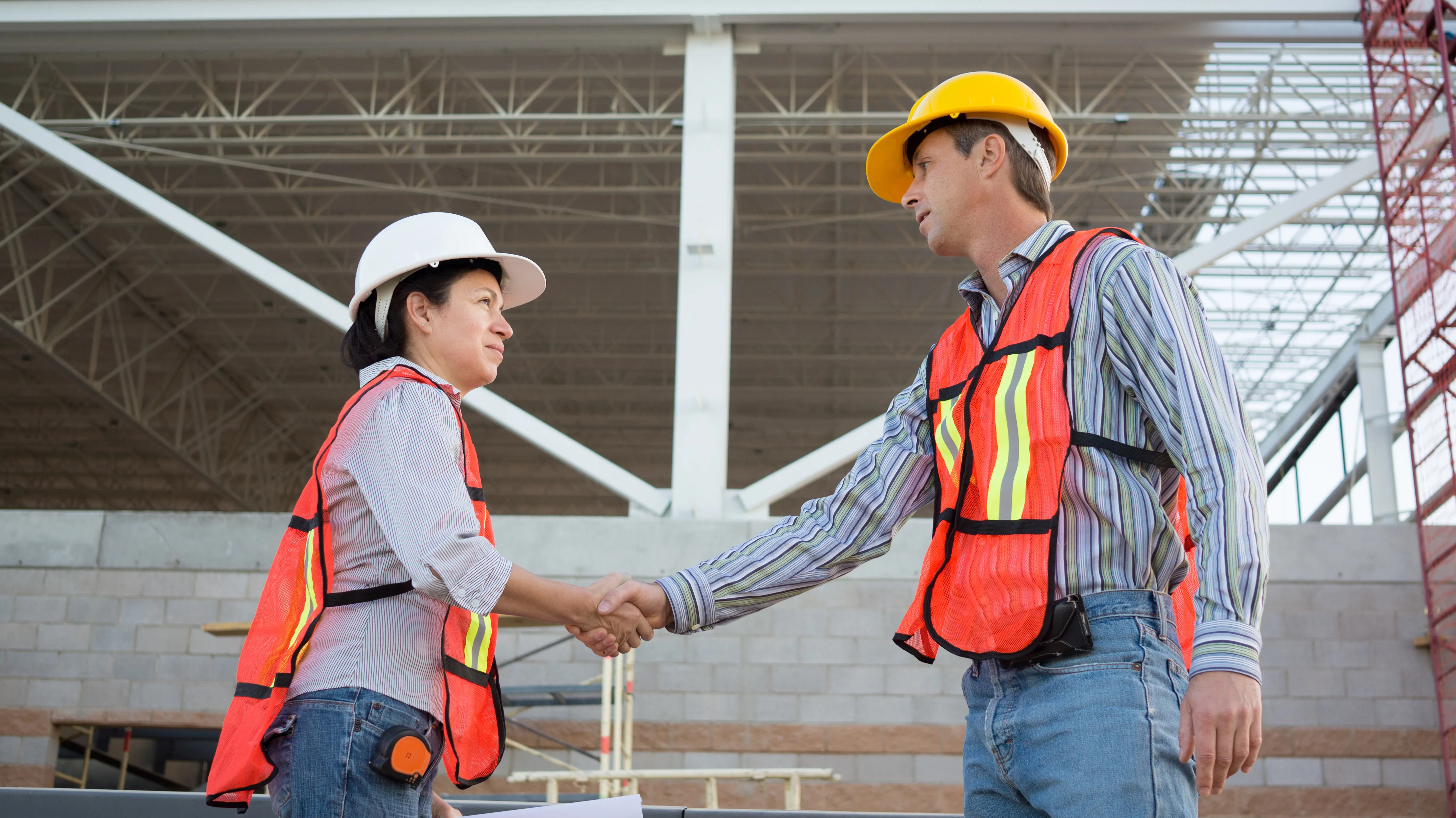 Two safety professionals in hard hats and high-visibility vests talking on a construction site