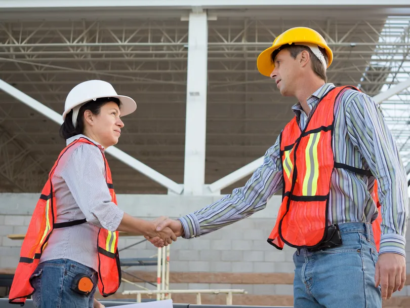 Two safety professionals in hard hats and high-visibility vests talking on a construction site